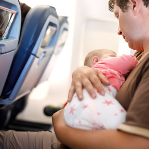 young tired father and his baby daughter sleeping during flight on airplane going on vacations. dad holding baby girl on arm. air travel with baby, child and family concept