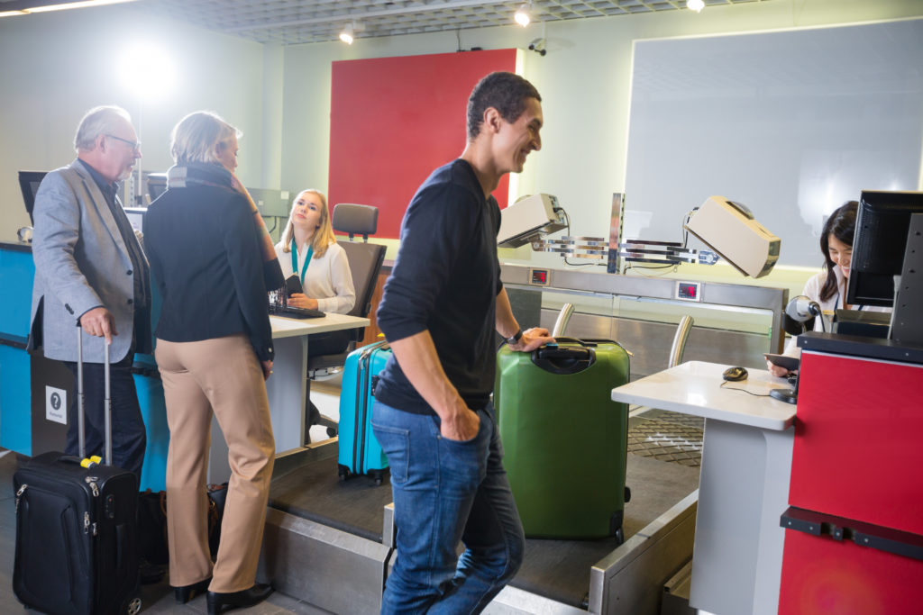 Des passagers masculins et féminins pesant leurs bagages au comptoir d'enregistrement de l'aéroport.