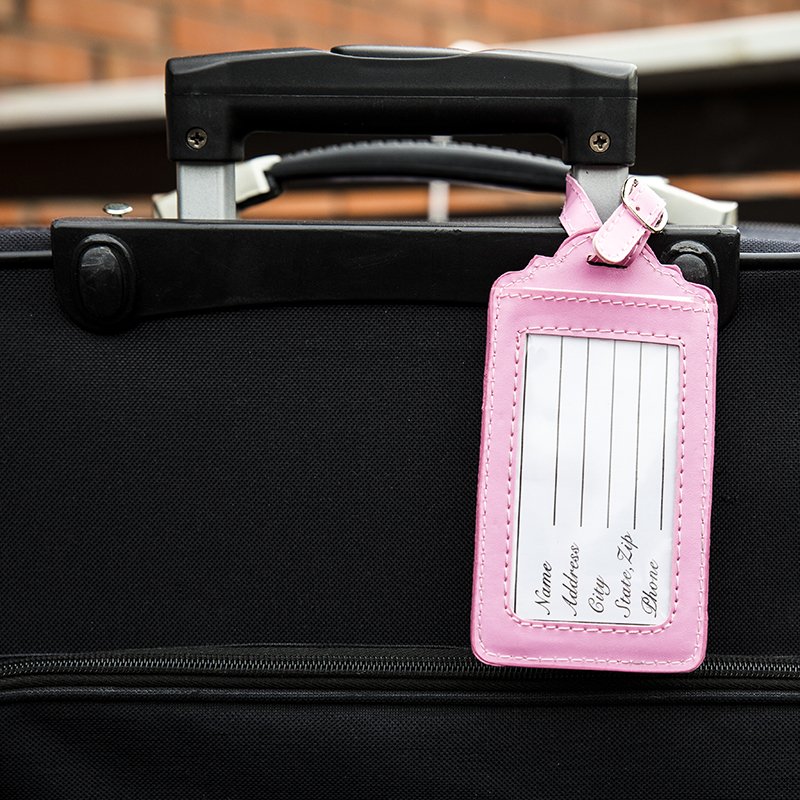 étiquette de bagage vide, rose et féminine, attachée à une valise noire