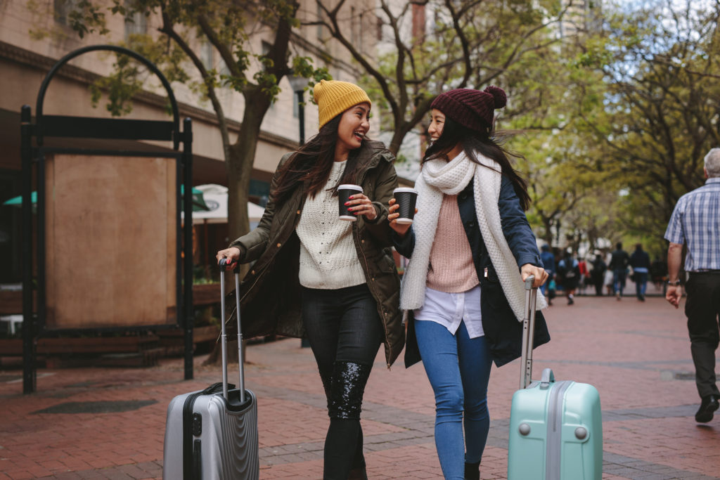 Deux femmes asiatiques marchant dans la rue avec des valises en buvant du café.