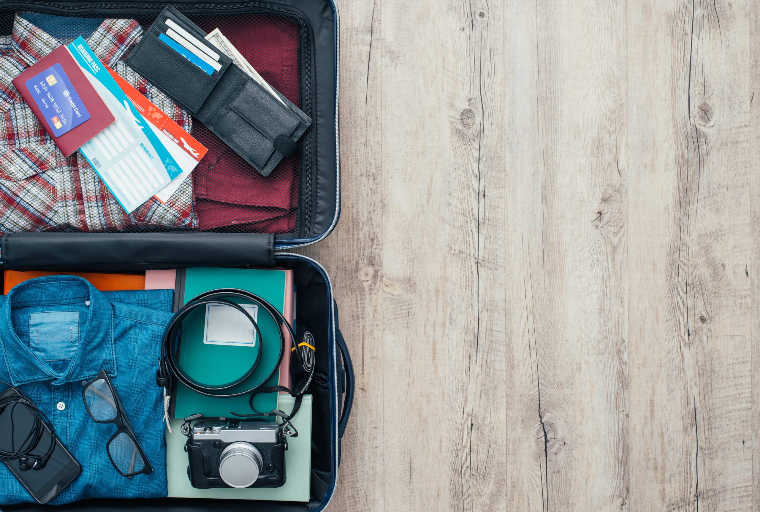 Une valise de voyageur ouverte avec des vêtements, des accessoires, une carte de crédit, des billets et un passeport, concept de voyage et de vacances, mise à plat.