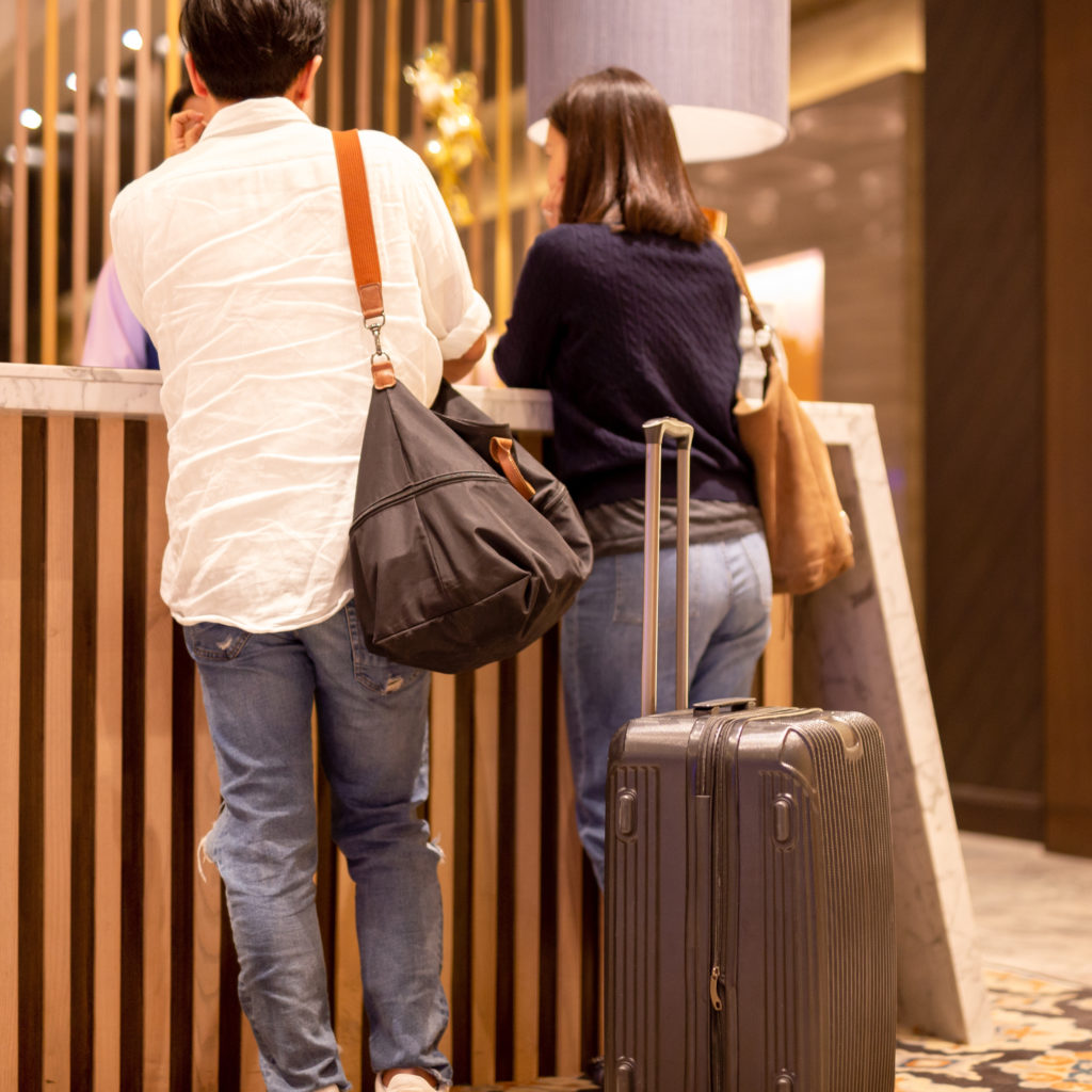 asian couple with suitcase checking in at hotel reception.
